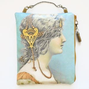 Può includere: Una pochette in tessuto blu e oro con una chiusura a zip e un fiocco. La pochette presenta un'illustrazione vintage di una donna con un copricapo dorato e una collana di perle.