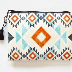 May include: A white zippered pouch with a black tassel. The pouch has a geometric pattern in shades of orange, blue, and black.