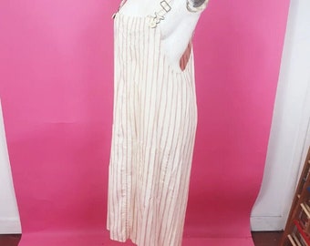 May include: A white and pink striped overall dress with thin straps and a button closure. The dress is made of a lightweight fabric and has a relaxed fit.