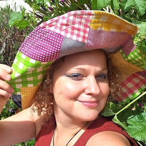Puede incluir: Un sombrero de ala ancha con un diseño de patchwork de cuadros vichy multicolores en tonos verde, rosa, amarillo y morado. El sombrero tiene una copa flexible y sin estructura, con un ala ancha que cae hacia abajo, confeccionado en algodón.