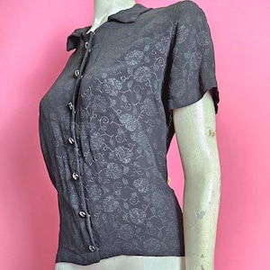 Blusa negra con estampado Volup de los años 40, mangas cortas y cierre de botones en la parte delantera.