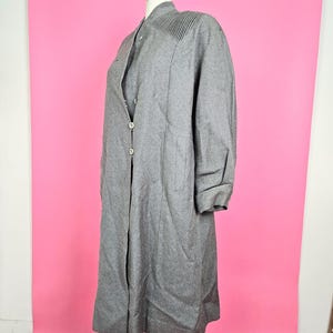 以下が含まれることがあります： 肩にプリーツのディテールが付いた、ボタン留めのロンググレーコートです。