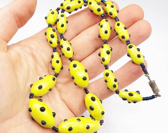 May include: A yellow necklace with black polka dots. The necklace is made of oval-shaped beads with a glossy finish.