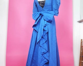 Puede incluir: Un vestido formal azul con un gran lazo en la espalda. El vestido tiene un escote en V y mangas cortas.