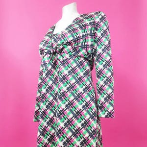 Peut inclure: Une robe à manches longues avec un motif à carreaux dans les tons de rose, vert, noir et blanc. La robe a un col en V et un nœud à la taille.