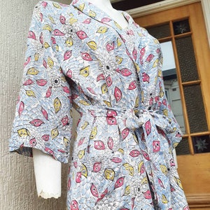 May include: A white robe with a blue and yellow floral pattern. The robe has a tie belt and long sleeves.
