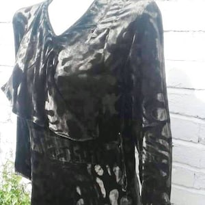 Op de afbeelding: Een zwarte fluwelen jurk met een wit en grijs abstract patroon. De jurk heeft een gerimpelde halslijn en lange mouwen.