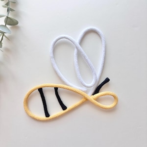 May include: A whimsical bee-shaped rope design. The bee's body is yellow with two black stripes, and the wings are white. The bee's stinger is black. The design is set against a white background.