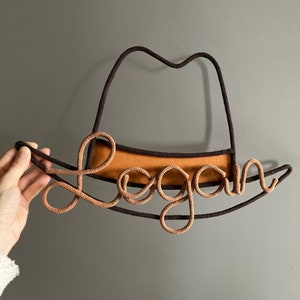 Custom name sign in the shape of a cowboy hat, crafted from cotton cord and sturdy wire.