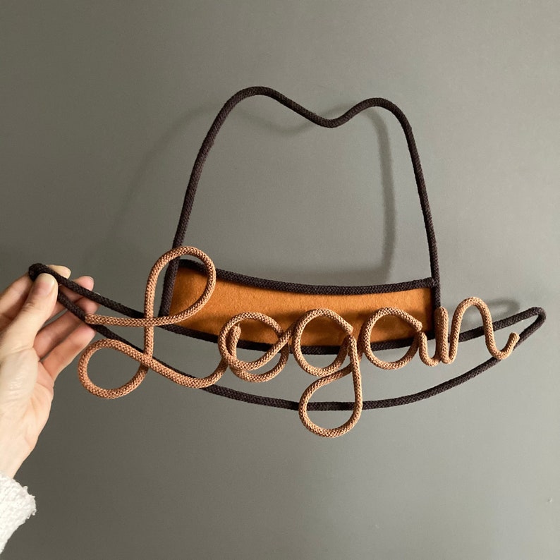 Custom name sign in the shape of a cowboy hat, crafted from cotton cord and sturdy wire.