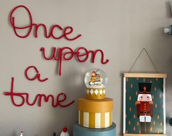 Puede incluir: Un letrero de pared de alambre rojo con el texto Once upon a time, una bola de nieve con figuras en un trineo, cajas de regalo redondas apiladas a rayas amarillas y azules, y un póster colgante de un cascanueces con figuras pequeñas.