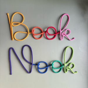 Book Nook sign displayed with fairy lights in cozy reading nook for nursery wall decor