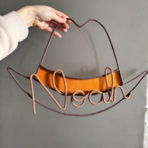 Western-inspired nursery name sign in a cowboy hat shape, handcrafted from rope and wire.