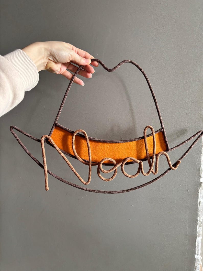 Western-inspired nursery name sign in a cowboy hat shape, handcrafted from rope and wire.