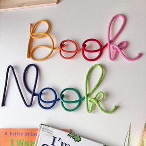 Rainbow Book Nook wall sign above kids reading corner with books
