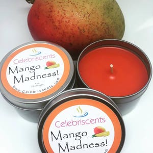 May include: Two silver candle tins with orange labels that read "Celebriscents Mango Madness!" and a mango fruit.