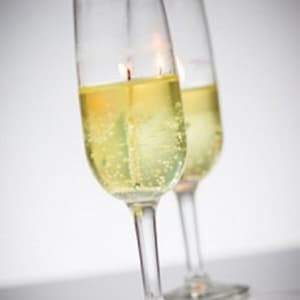 May include: Two clear glass champagne flutes filled with yellow liquid and a floating candle in each.