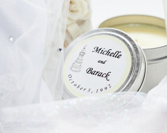 May include: A white candle in a silver tin with a label that reads "Michelle and Barack October 3, 1992". The label also features a small illustration of a wedding cake.
