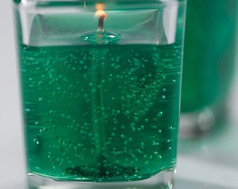May include: Two square glass candles filled with green gel and small bubbles. The candles have a lit wick and are set against a white background. The candles are a decorative item.
