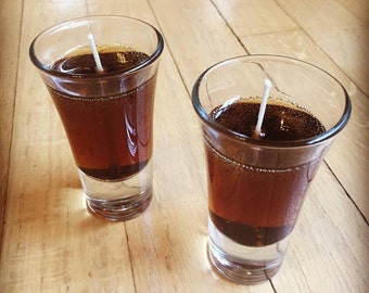 May include: Two clear glass shot glasses filled with brown gel candles with white wicks.