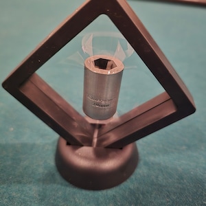 May include: A silver socket wrench is displayed in a black diamond-shaped frame with a black base. The socket wrench is 1/2 inch.