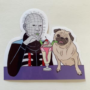 May include: A sticker featuring a cartoon illustration of a man with a grid-like face and a pug dog, both drinking milkshakes with straws. The man is wearing a black and red jacket and the pug is sitting on a purple table.
