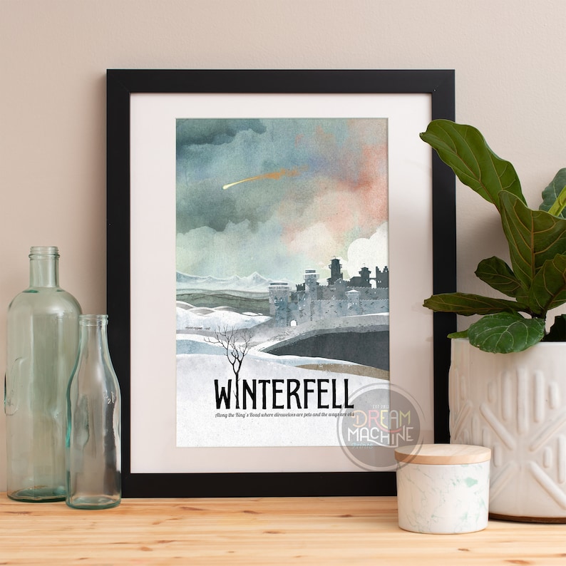 May include: Framed art print featuring a watercolor illustration of Winterfell, with a castle, snowy landscape, and a dramatic sky. The print includes the word "WINTERFELL" and the Dream Machine logo.