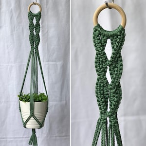 May include: A green macrame plant hanger with a wooden ring at the top. The plant hanger is designed to hold a small white pot with a green plant. The macrame design features a woven pattern and a tassel at the bottom.