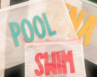 Puede incluir: Tres bolsas de malla con cremallera con las palabras "POOL", "SWIM" y "LAVA" en letras grandes y coloridas. La bolsa "POOL" tiene letras turquesas con un contorno naranja. La bolsa "SWIM" tiene letras rojas. La bolsa "LAVA" tiene letras amarillas.