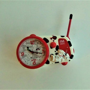 Könnte beinhalten: Ein rotes und weißes Dalmatiner-Themen-Radiowecker mit einem schwarz-weißen Zifferblatt und einer schwarzen Antenne. Das Zifferblatt der Uhr hat einen weißen Hintergrund mit schwarzen Zahlen und einem schwarzen Zeiger. Das Radio hat ein schwarz-weißes Zifferblatt mit den Worten "FM RADIO" in rot.