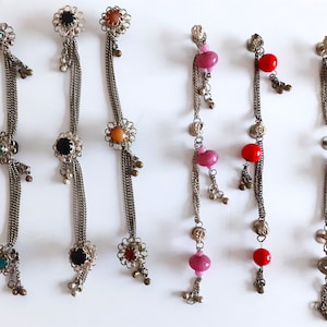 Könnte beinhalten: Satz mit sechs silberfarbenen Haarklammern mit baumelnden Anhängern. Die Anhänger bestehen aus einem schwarzen, grünen und orangefarbenen Stein, einer rosa Perle und einer roten Perle.