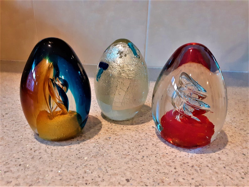 3 glass egg paperweights from the 1980s. 
1  Flamboyant colours in tongues of flame and sapphire
2 Murano glass with silver leaf interior and pieces of blue
3 Silver twist rises from  bright vermillion base 
All 12cm tall, and  under 1kg each.