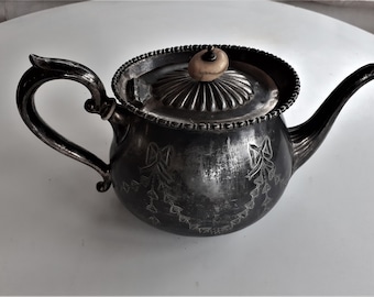 Puede incluir: Una tetera de plata con un diseño ornamentado y un pomo de hueso en la tapa. La tetera tiene un patrón floral y un acabado ligeramente deslustrado.