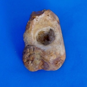 May include: A light brown stone with a smooth, round hole in the center. The stone has a rough, uneven texture and is likely a natural object.