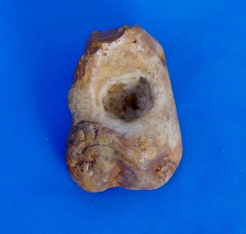 May include: A light brown stone with a smooth, round hole in the center. The stone has a rough, uneven texture and is likely a natural object.