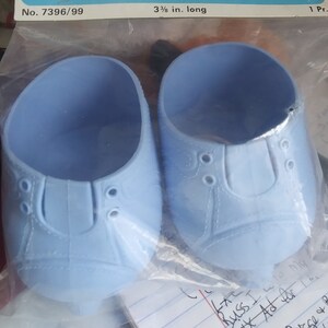 May include: A pair of light blue Doll Baby roller skates, 8.57 cm long, in their original packaging. The packaging features the text "The Original DOLL BABY ROLLER SKATES".