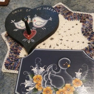 May include: Two hand-painted wooden signs with a heart and a bird theme. The heart-shaped sign reads "Here is my heart" and features two birds kissing. The other sign features a blue bird with yellow flowers.