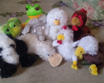 May include: A collection of eight plush toys, including a green frog, a white chicken, a brown chicken, a white duck, a gray elephant, a white penguin, a black and white panda, and a brown and white duck.