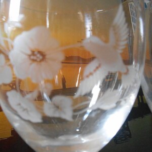May include: A clear glass wine glass with an etched design of a hummingbird and a flower. The glass is partially filled with liquid.