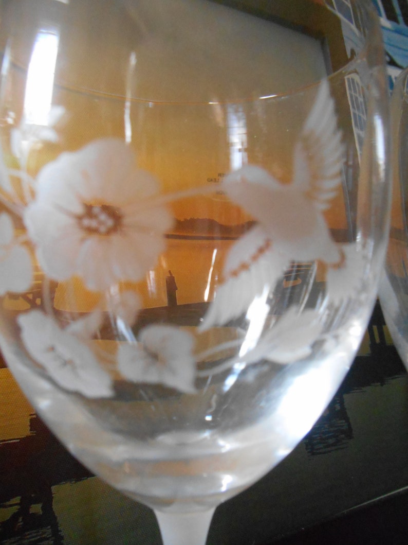 May include: A clear glass wine glass with an etched design of a hummingbird and a flower. The glass is partially filled with liquid.