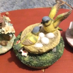 Puede incluir: Un juego de tres tazas de cer&aacute;mica con un esmalte moteado de color crema. Cada taza presenta un dise&ntilde;o pintado a mano diferente: un patr&oacute;n floral azul, una hoja verde y un sol amarillo. Las tazas tienen una forma simple y redondeada.