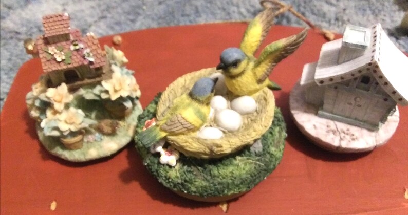 Puede incluir: Un juego de tres tazas de cer&aacute;mica con un esmalte moteado de color crema. Cada taza presenta un dise&ntilde;o pintado a mano diferente: un patr&oacute;n floral azul, una hoja verde y un sol amarillo. Las tazas tienen una forma simple y redondeada.