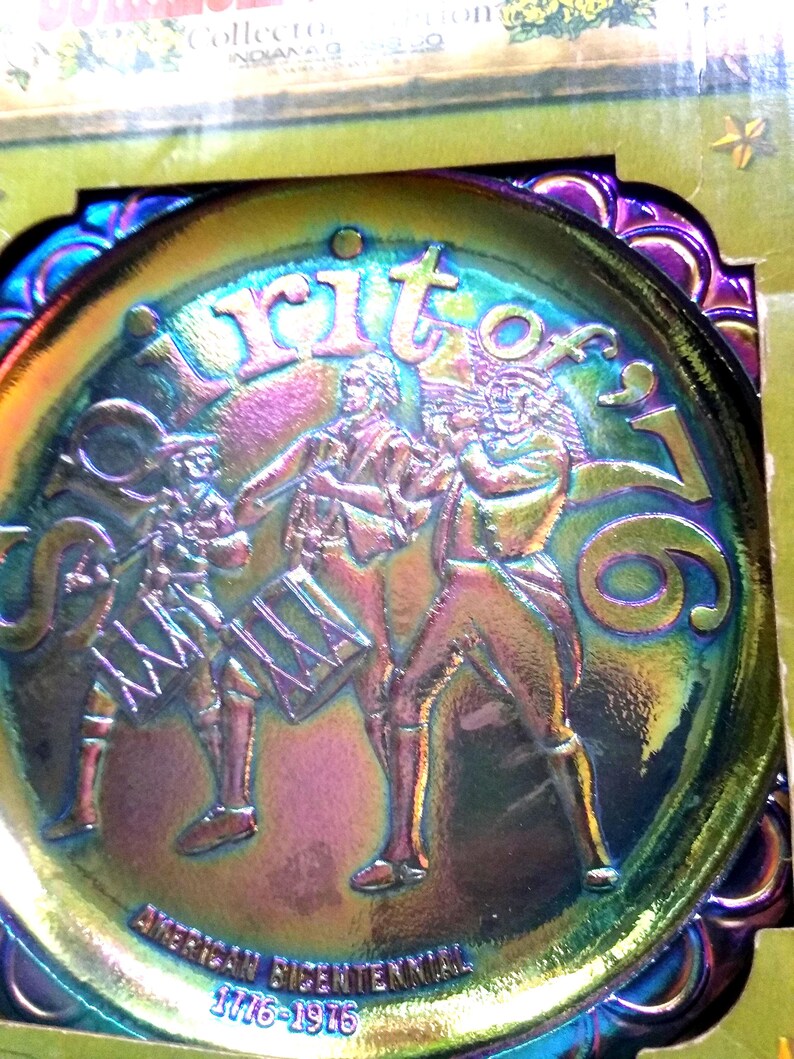 Puede incluir: Plato decorativo iridiscente con tem&aacute;tica patri&oacute;tica. El plato presenta un relieve de tres figuras tocando instrumentos, con las palabras "Spirit of '76" y "American Bicentennial 1776-1976" inscritas.