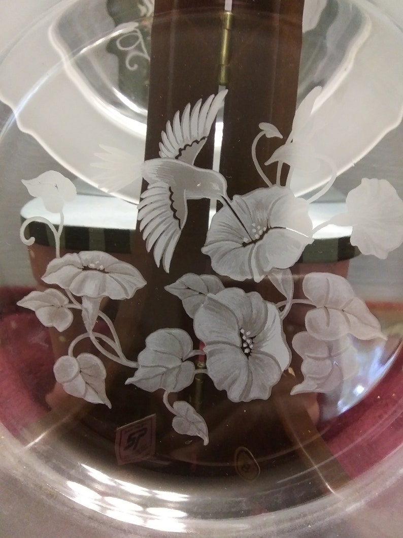 May include: A clear glass plate with an etched design of a hummingbird and flowers. The design is in white and is on a brown background.