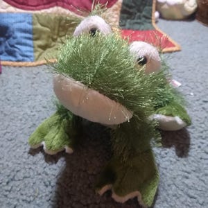 May include: Green fuzzy frog plush toy with white belly and large black eyes.