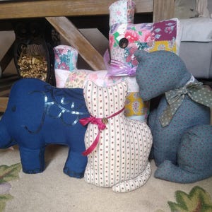 May include: Four handmade stuffed animal toys: a blue elephant with sequins, a white and pink striped cat, a blue cat with a green bow, and a multi-colored patchwork cat.