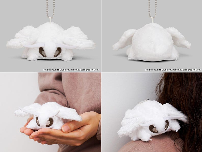 May include: White plush toy of a moth with a silver chain attached. The moth has large wings and a small, round body. The toy is shown in different positions, including hanging from the chain and being held by a person.