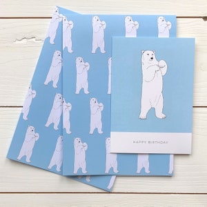 May include: A blue and white birthday card with a polar bear holding a snowball. The card has the text "Happy Birthday" printed on the front.