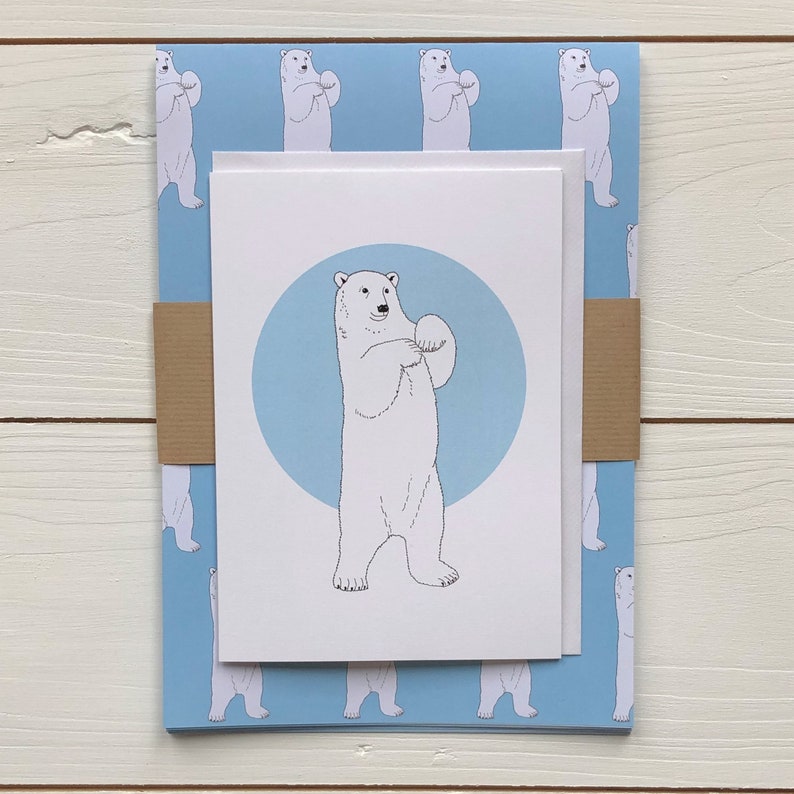 May include: A white card with a blue circle and a black and white illustration of a polar bear standing on its hind legs. The card is on top of a blue wrapping paper with a repeating pattern of polar bears.