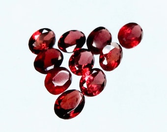 May include: A group of ten oval-shaped, red gemstones. The gemstones are arranged in a triangular pattern on a white background.